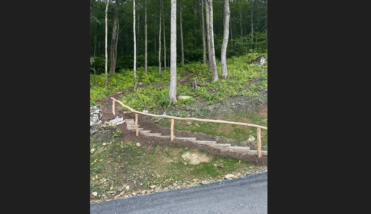 A peaceful forest pathway featuring wooden steps surrounded by tall trees, evoking a sense of exploration and tranquility. The path invites guests to hike or stroll into nature right from the property.