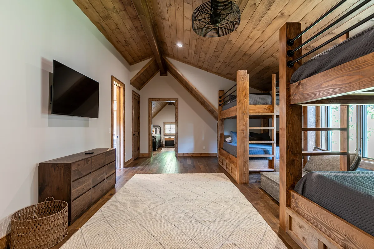 A warm, inviting bunk room with wooden bunk beds, a TV, woven basket, and area rug. The space is designed for group sleepovers, movie nights, and casual hanging out, making it ideal for kids and family fun.