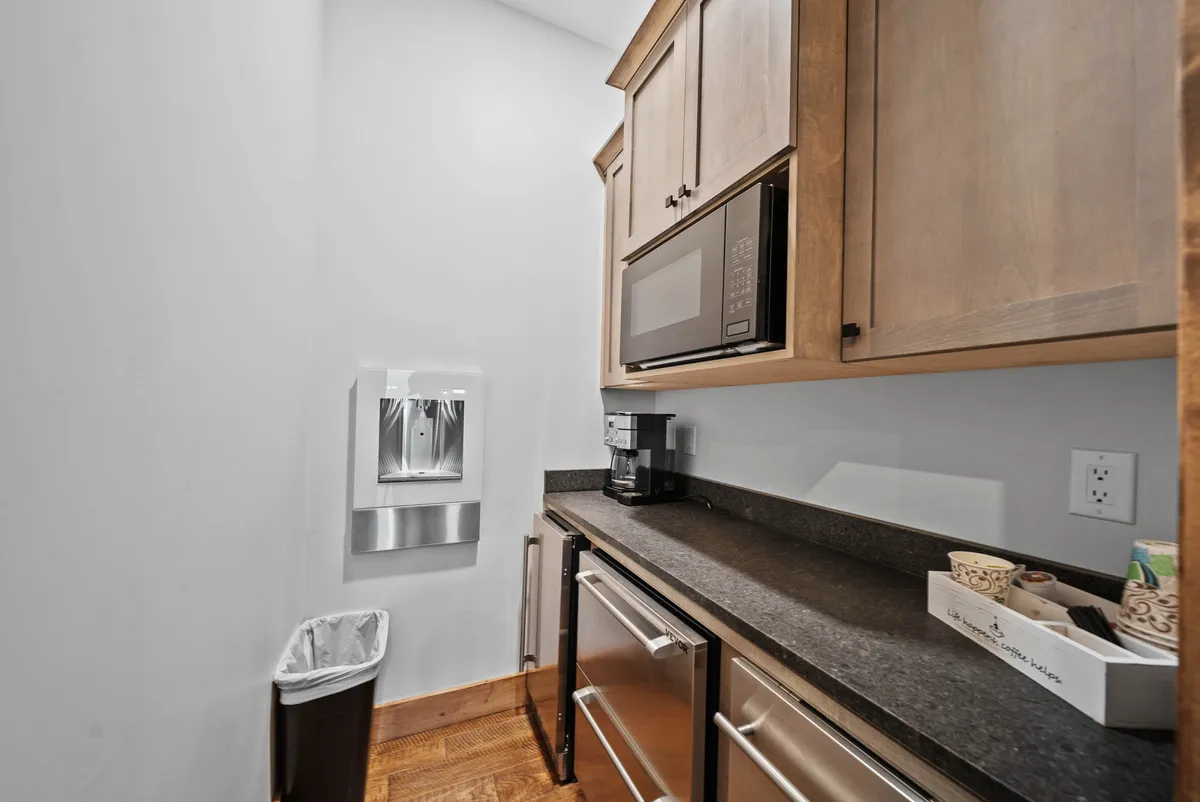 A kitchenette with kitchen cabinets, microwave, coffee maker, water dispenser, and countertop space, set in a practical and accessible layout.