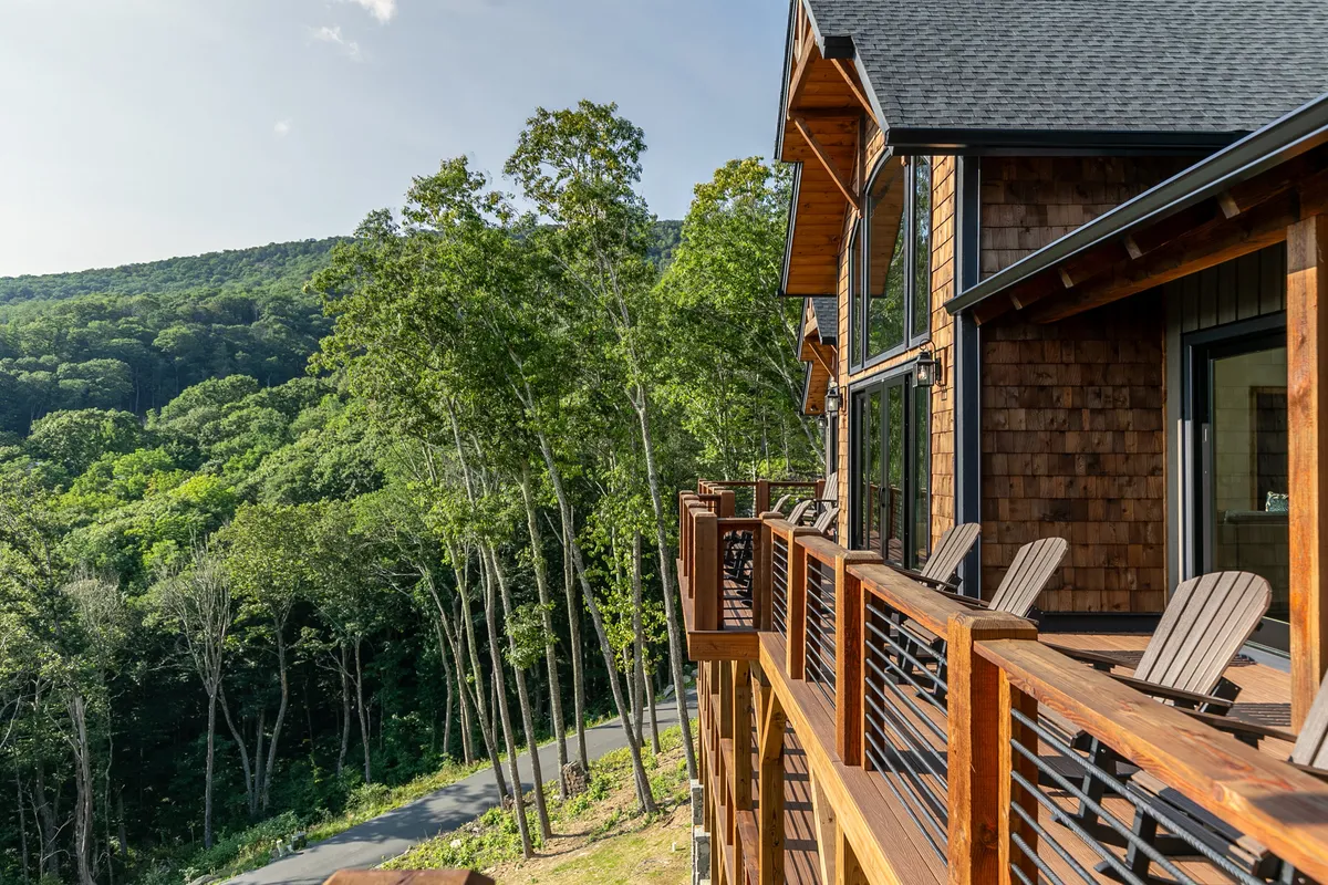 A spacious wooden deck furnished with Adirondack chairs, offering an unobstructed view of the surrounding mountains and treetops. The setting is ideal for relaxing after a day of activity, soaking up the tranquil mountain atmosphere, and observing wildlife or sunsets.