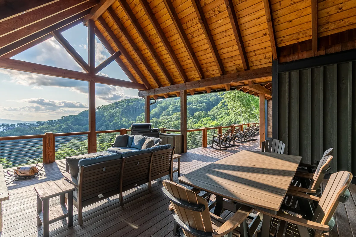 An inviting deck with a wooden dining table, comfortable seating area, and a grill overlooking lush greenery. The scene is set for group gatherings, barbecues, and special celebrations with a breathtaking backdrop.