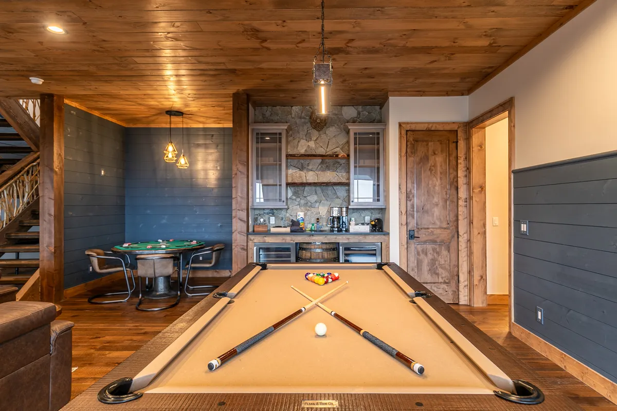 A vibrant game room scene with a pool table, poker table, wooden cabinetry, and stone backsplash. The setup is perfect for friendly competition and socializing, with multiple games visible in one shot.